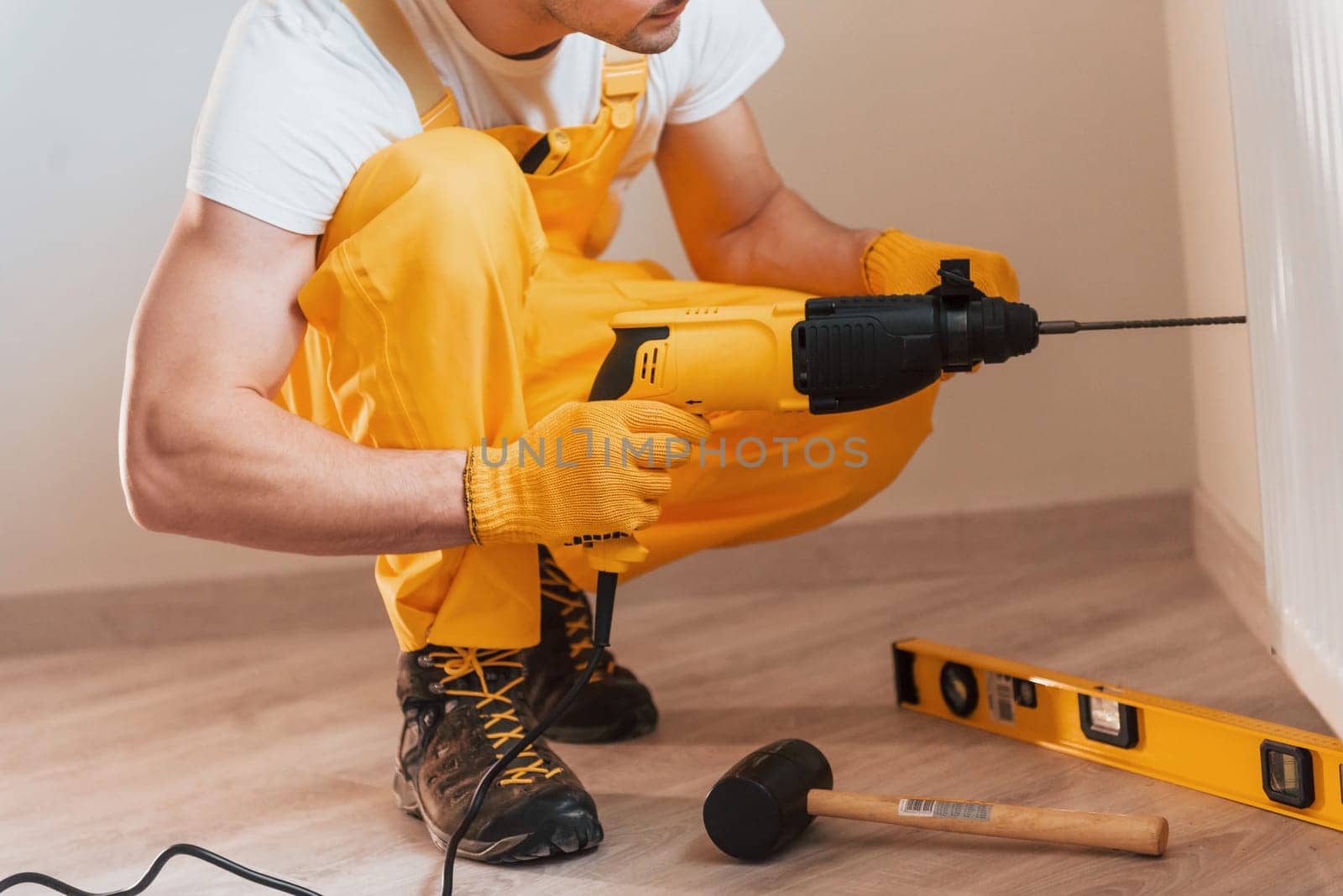 Handyman in yellow uniform works indoors by using hammer drill. House renovation conception by Standret