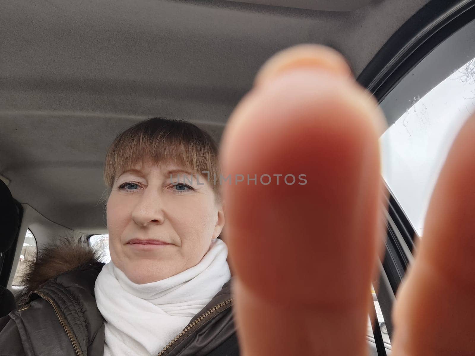 Portrait of adult cute funny blonde woman in warm clothes taking a selfie inside the car and driving it. The concept of a pleasant trip in spring, autumn, winter by keleny