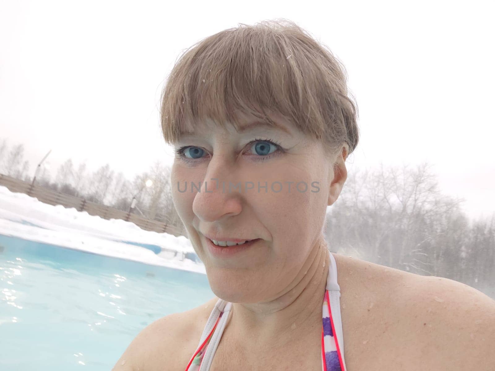 Adult mature woman takes a selfie in a pool with warm hot termal mineral water in winter and white snow around. Wellness center and the concept of health care. Travel, recreation, medicine and rest by keleny