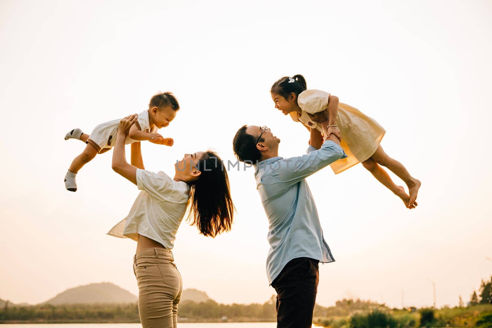 A happy family enjoys a playful moment in a summer field, as the dad and mom throw their child up into the blue sky. The cheerful family looks on with joy and love, Family day