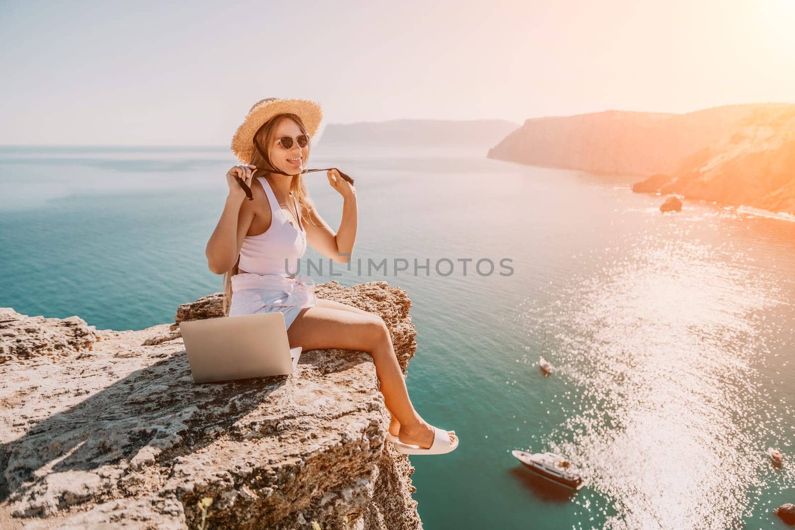 Digital nomad, Business woman working on laptop by the sea. Pretty lady typing on computer by the sea at sunset, makes a business transaction online from a distance. Freelance, remote work on vacation