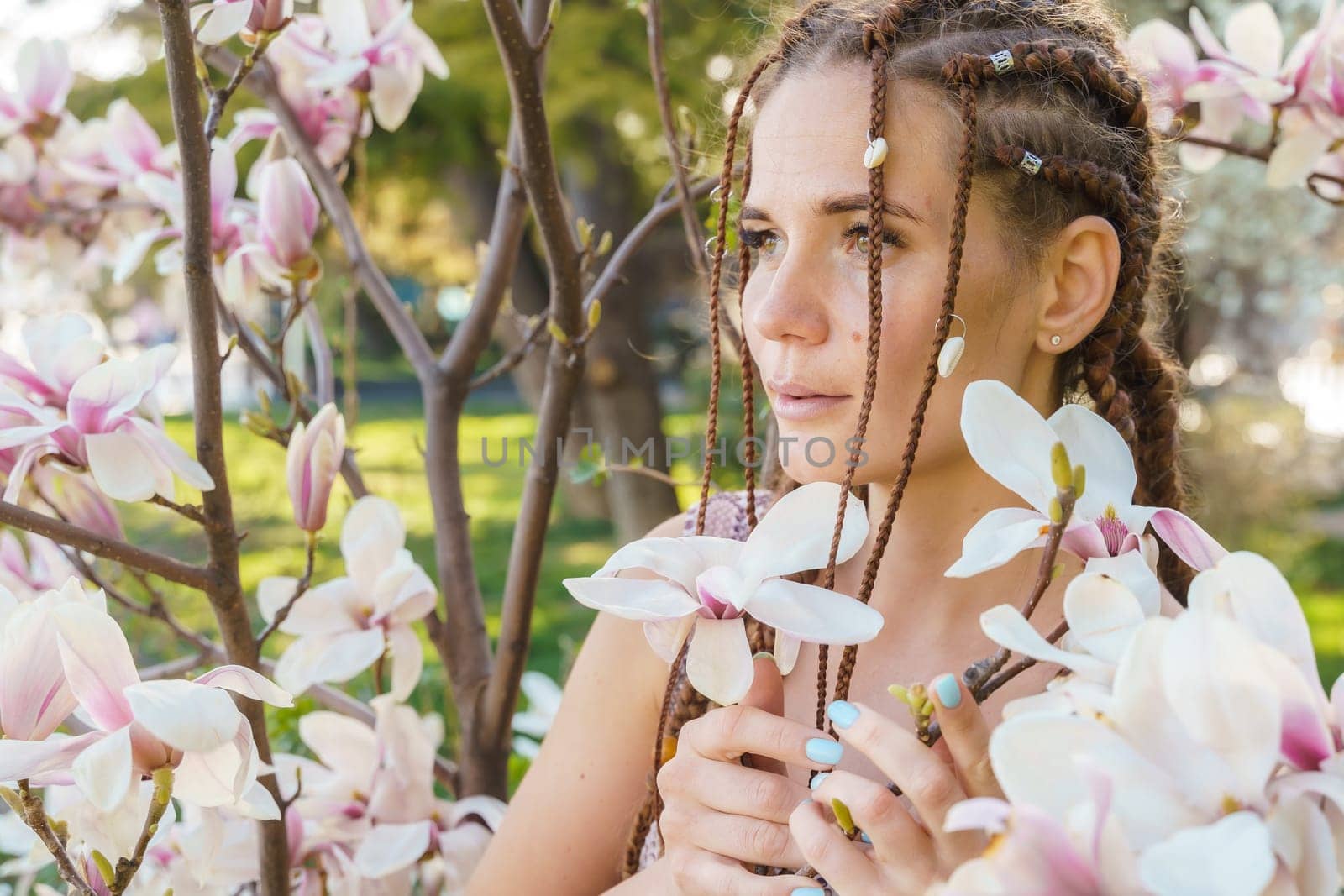 Magnolia flowers. Happy woman enjoys by blooming magnolia tree and sniffs it flowers with closed eyes in spring garden. Portrait