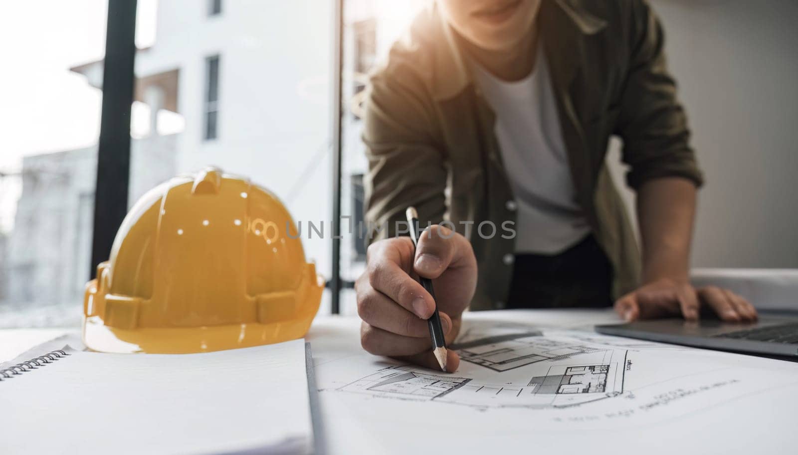 Engineers holding a pen pointing to a building and drawing outlay construction plan as guide for builders with details. by wichayada