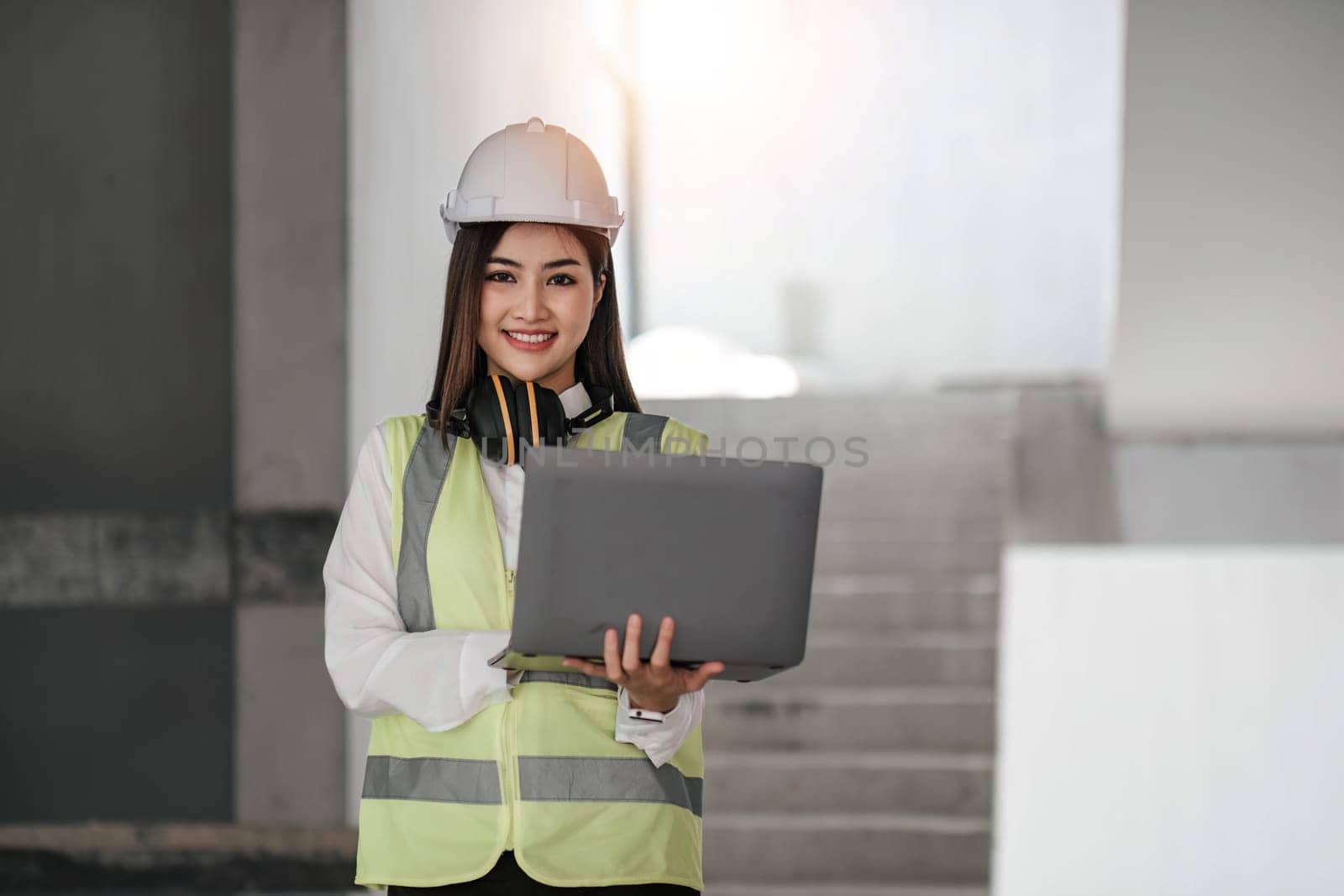 Portrait of Happy professional construction engineer woman holding laptop and wearing the safety helmet at the building site place background, industrial engineering concept..