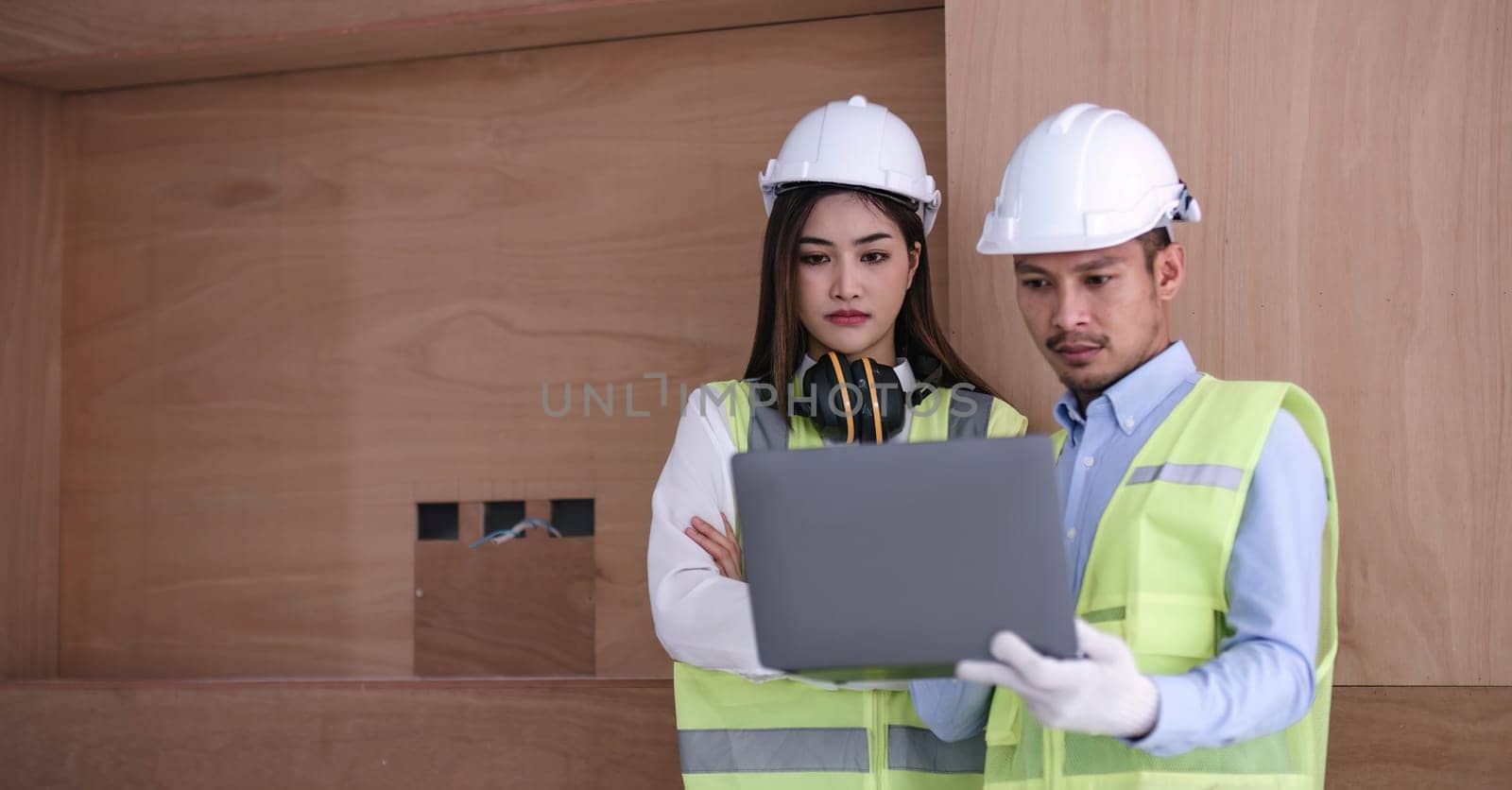 Structural engineer and architect dressed in reflective vests discuss the construction process by the chart and laptop...