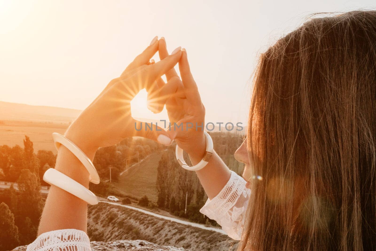 Romantic beautiful bride in white dress posing with sea and mountains in background. Stylish bride standing back on beautiful landscape of sea and mountains on sunset