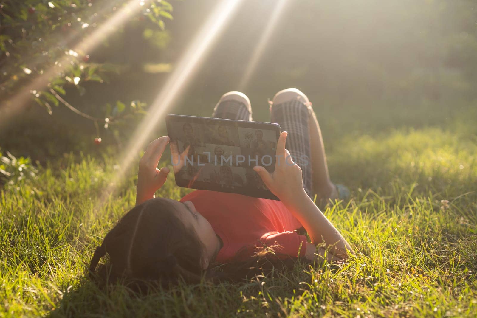 Girl on the grass with a tablet chat in her hands in the garden.