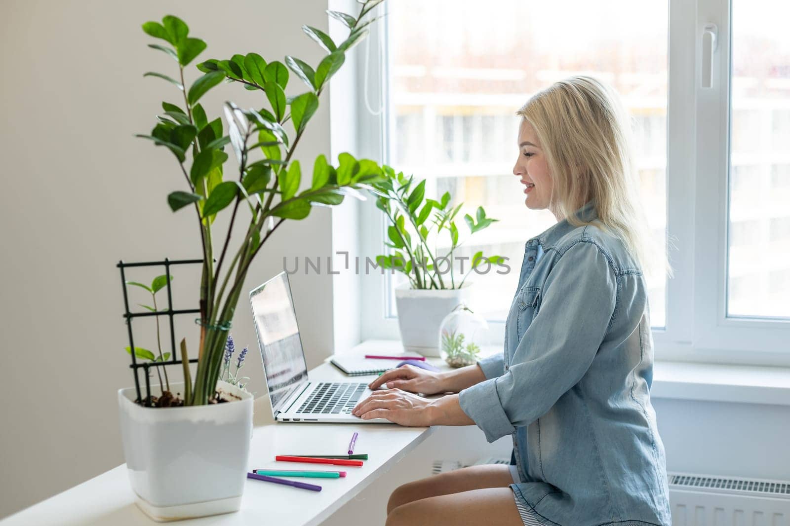 Woman on remote work or online education, using laptop computer, making notes, indoors at office or home at daytime. Online business, young professional at workplace. Working from home.