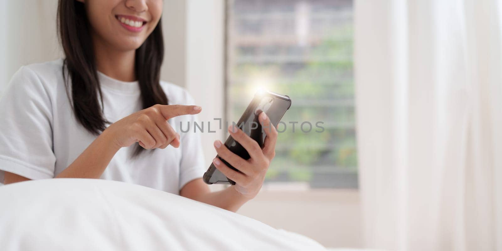 Smiling young asian woman using smart phone in bedroom at home. lifestyle, woman lying on bed.
