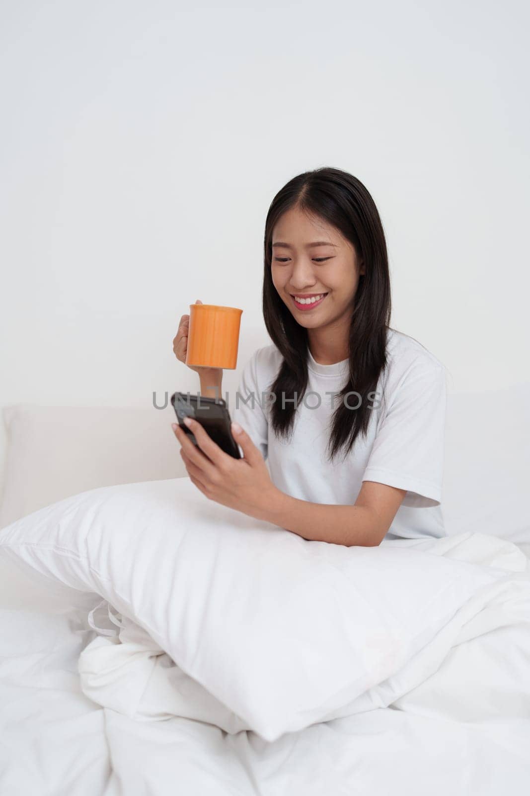 Smiling young asian woman using smart phone in bedroom at home. lifestyle, woman lying on bed by itchaznong