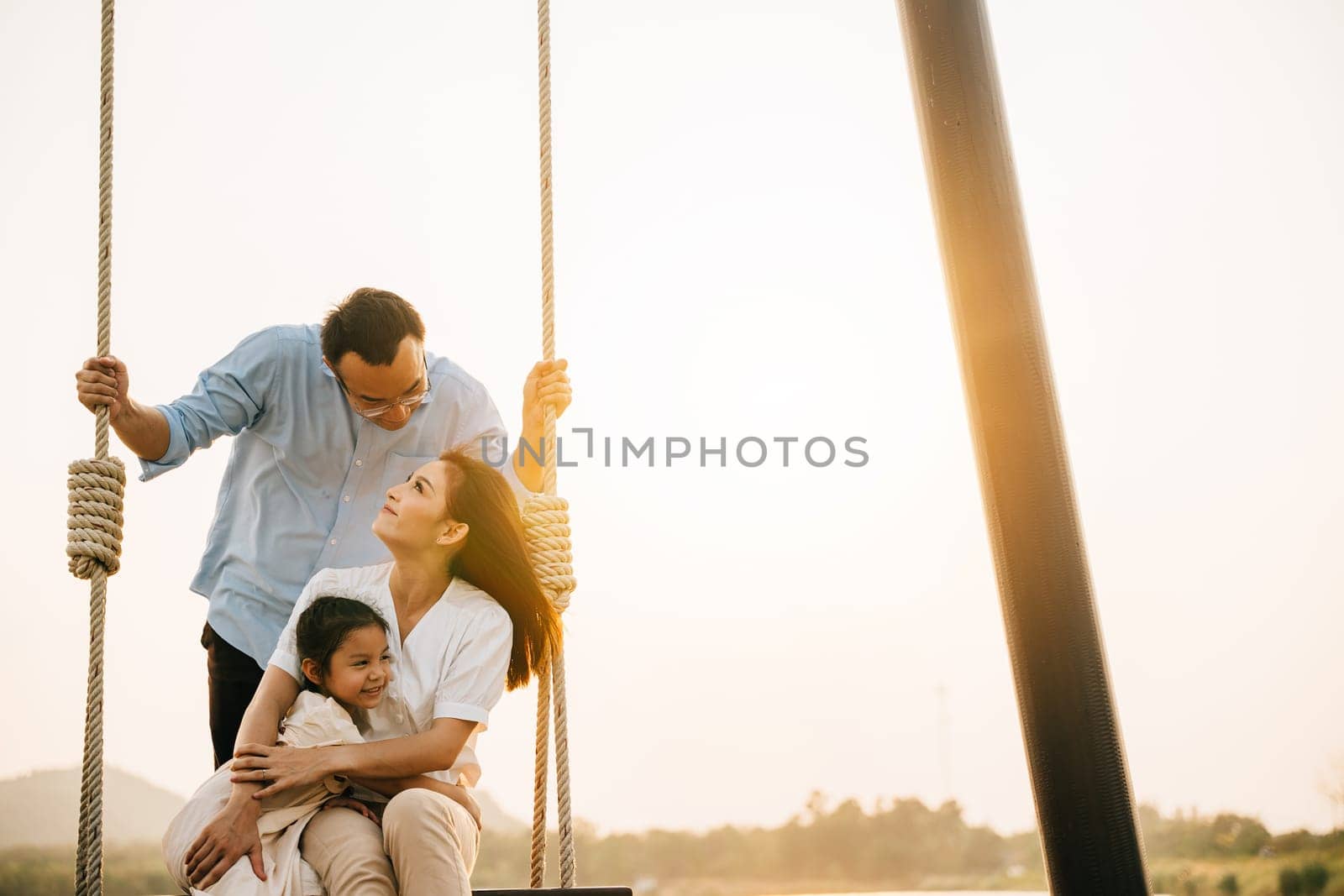 An Asian family having fun in the garden, with the father and daughter swinging on a sunny spring day, feeling the happiness and the love of a playful family, Happy Family Day