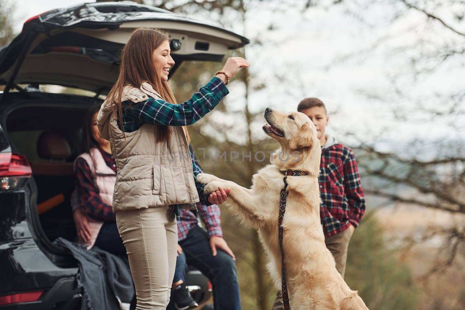 Happy family have fun with their dog near modern car outdoors in forest.