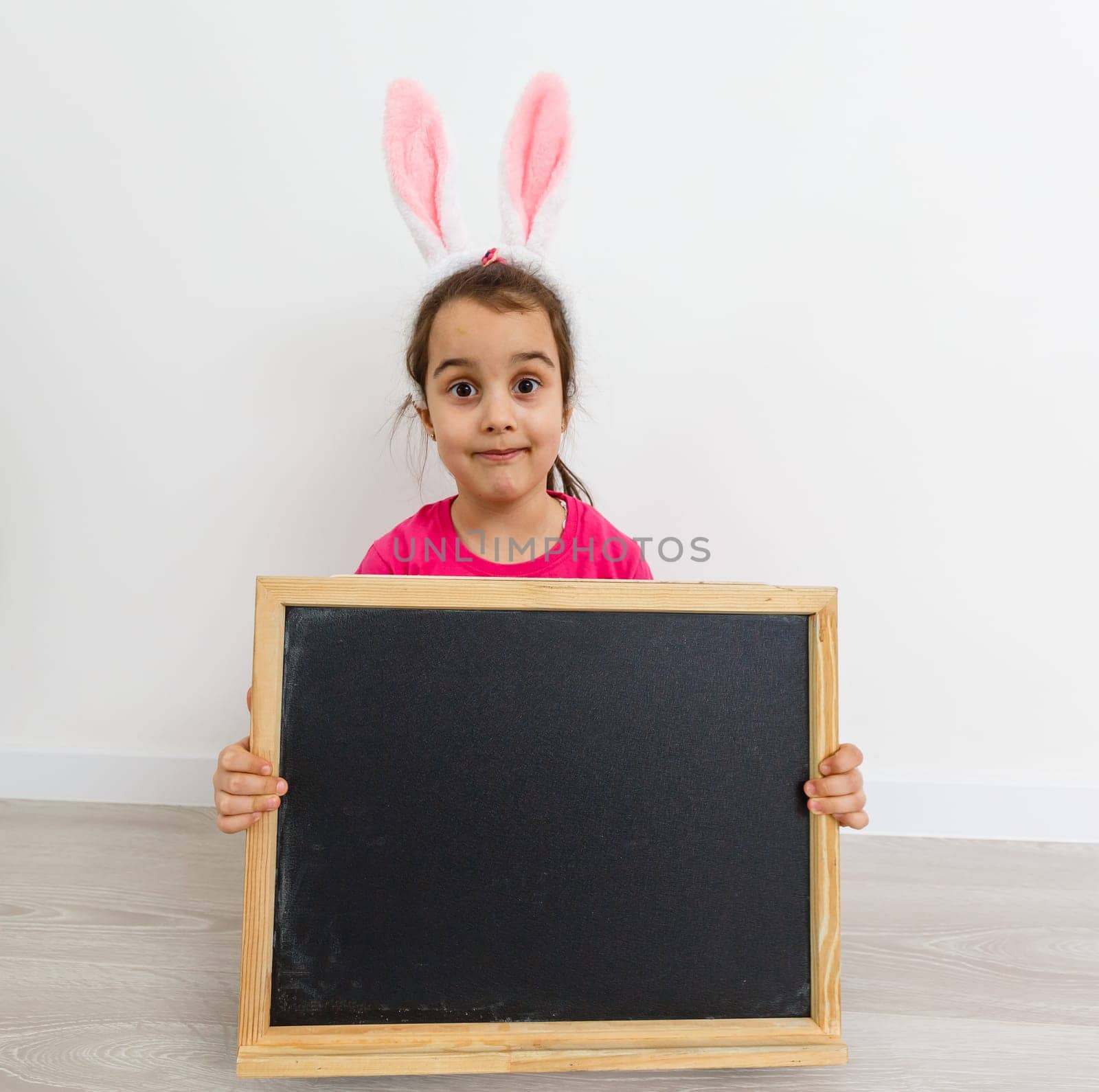 Very angry little girl wearing bunny ears sitting on a floor at home