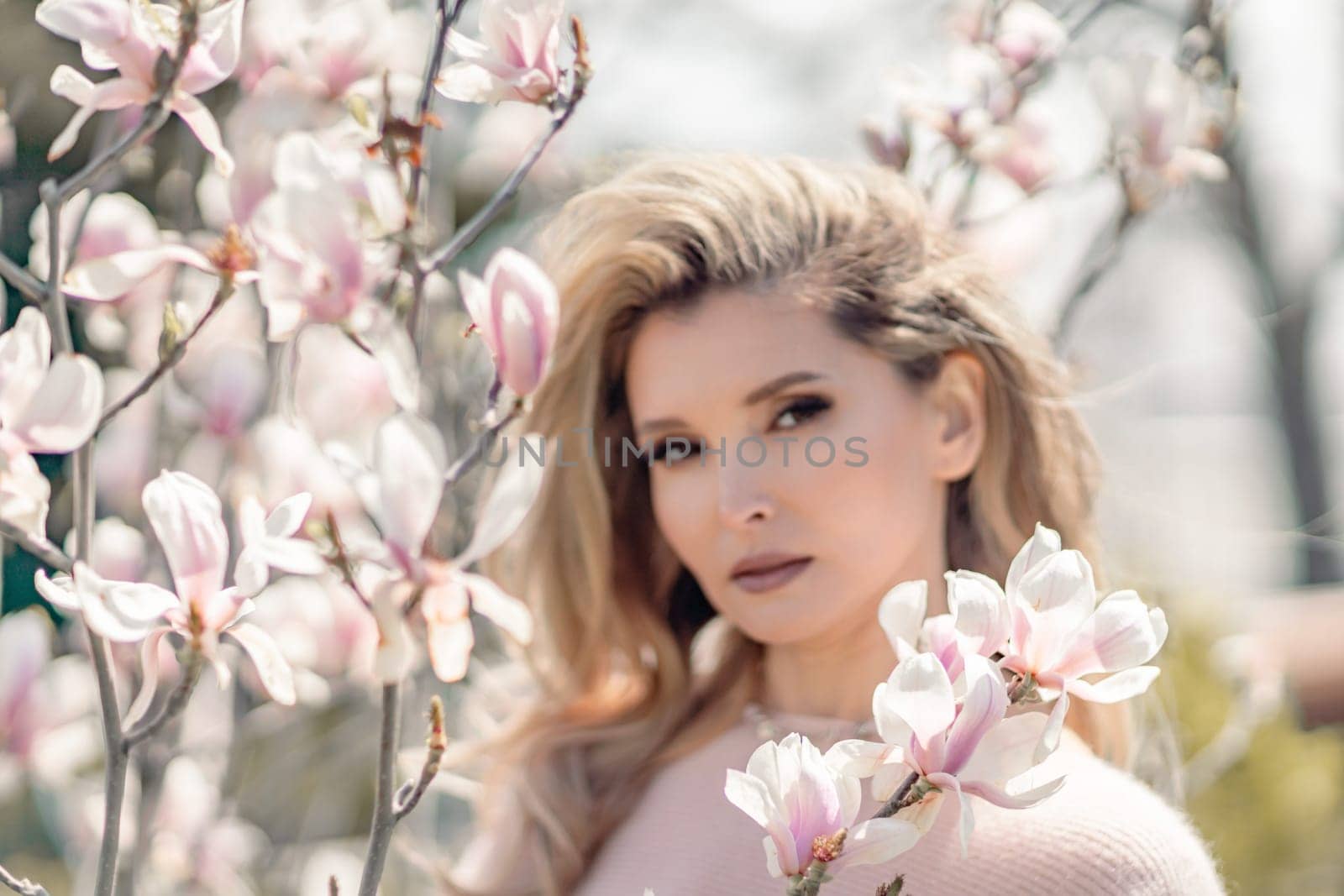 Portrait of a beautiful happy middle aged woman enjoying the smell in a blooming spring garden. Beautiful magnolia bushes, large flowers. by Matiunina