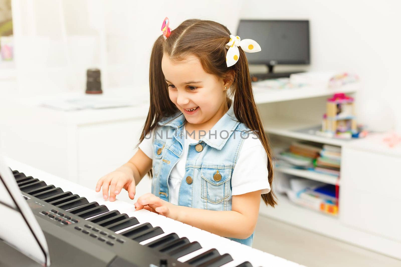 Beautiful little kid girl playing piano in living room or music school. Preschool child having fun with learning to play music instrument. Education, skills concept by Andelov13