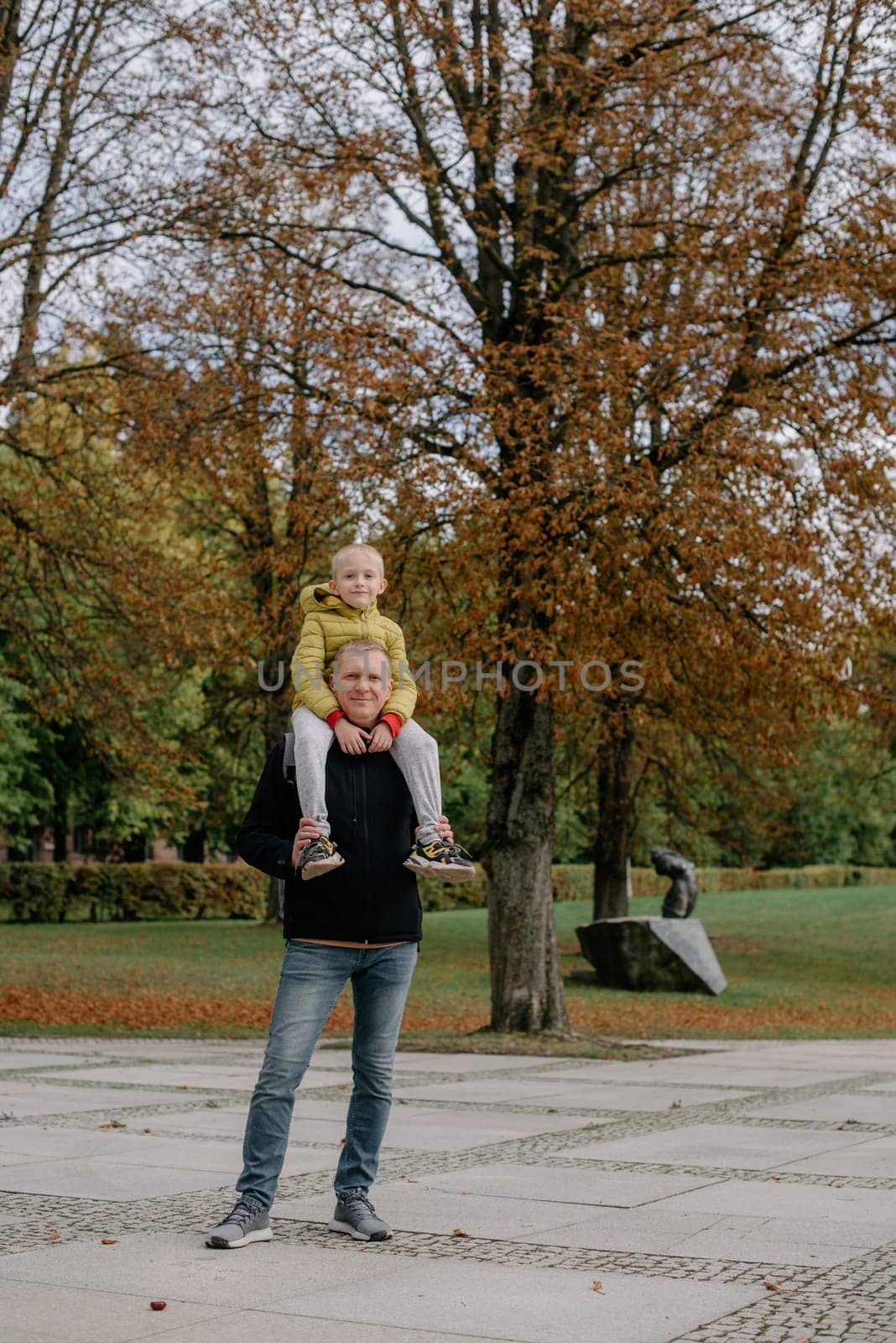 Dad holds on his son's shoulders. Beautiful family is spending time together outside. Dad and his little son are having fun on a roof terrace with view on a city. Sitting on father's shoulders and smiling.