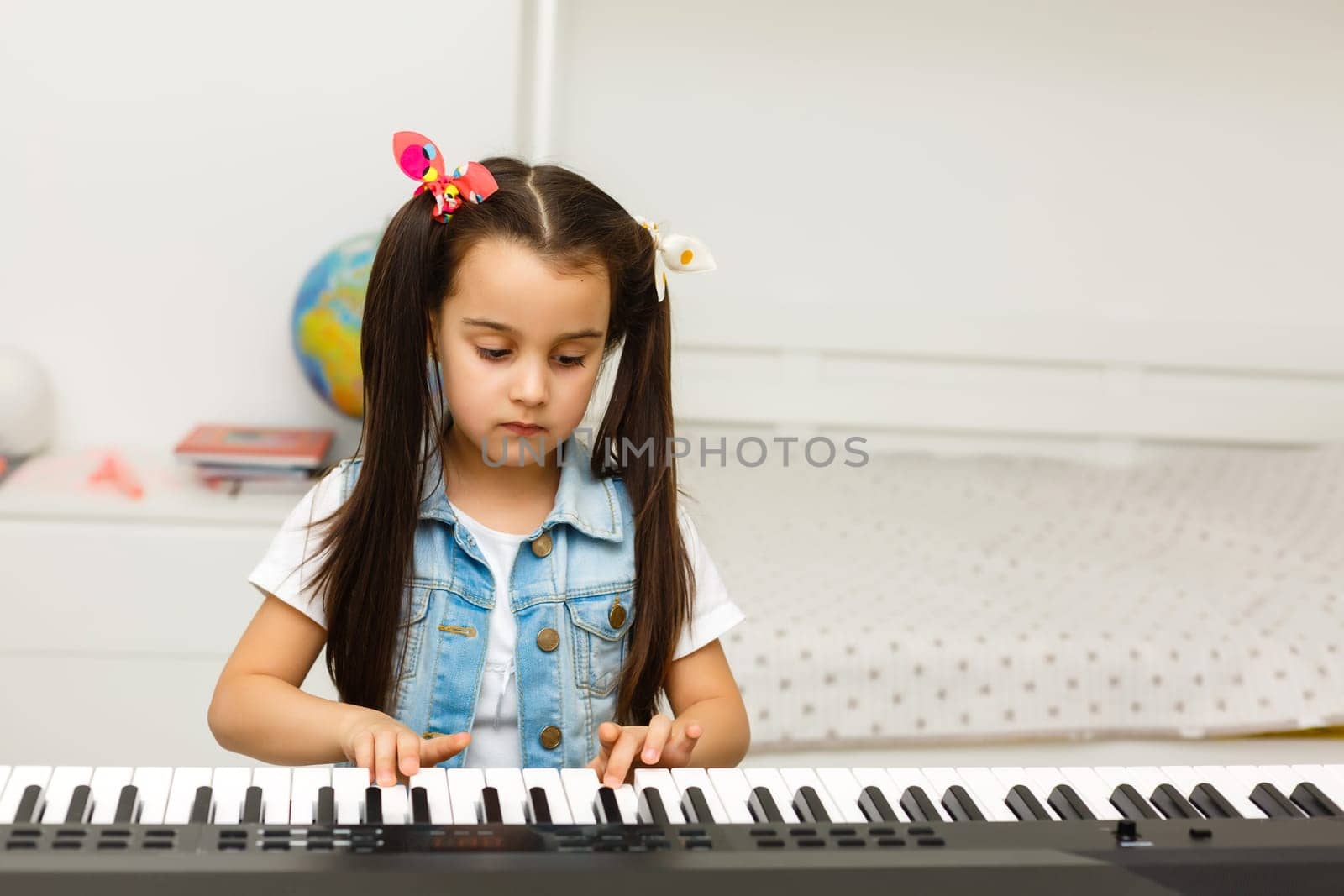 Cute little girl plays on piano, synthesizer. Training. Education. School. Aesthetic training. Elementary classroom.