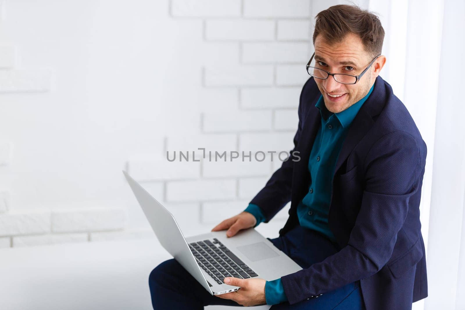 Handsome young man wearing glasses and working with touchpad while sitting on the couch in office by Andelov13