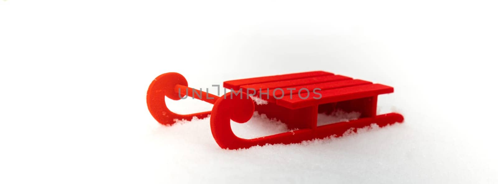 Small Red sled on snow background in beautiful winter day. Copy space for text. Mock up for product greeting card or wallpaper. Christmas holiday concept.
