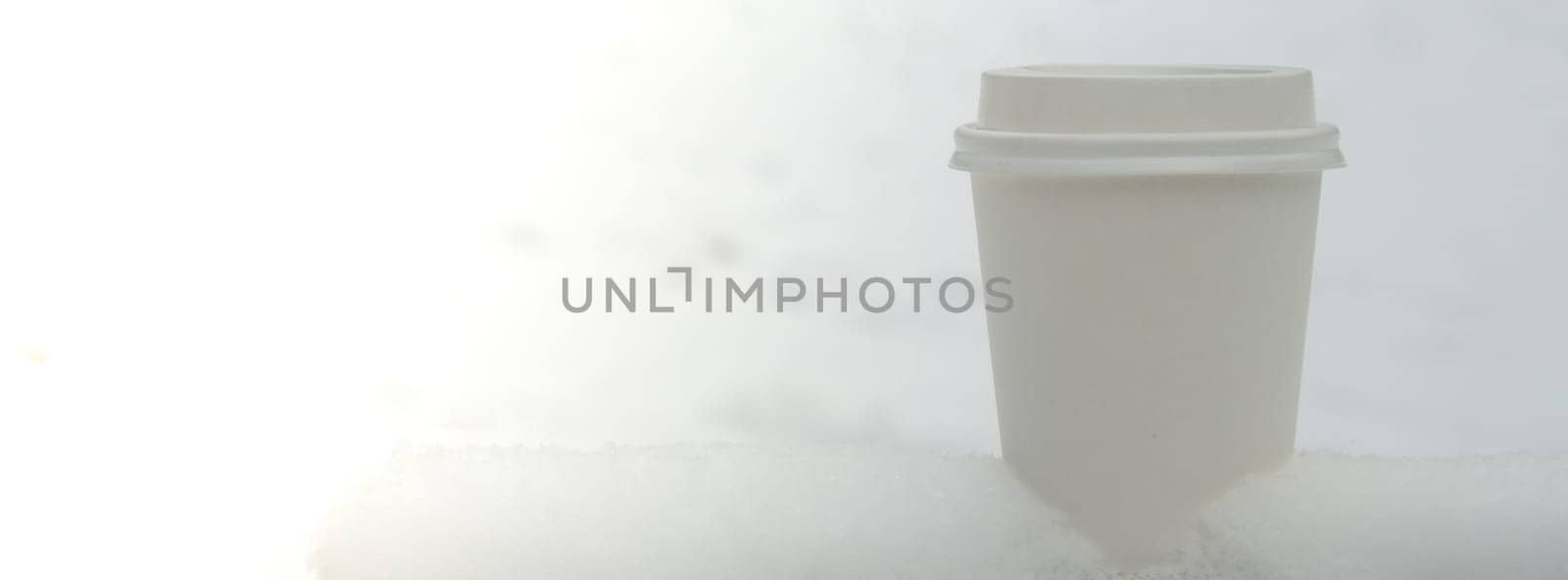 Hot warming drink in Eco paper cup. Mock up Cardboard coffee or tea Cup in the snow in winter day. Copy space Creative trendy zero waste recycle cup white snow-covered field