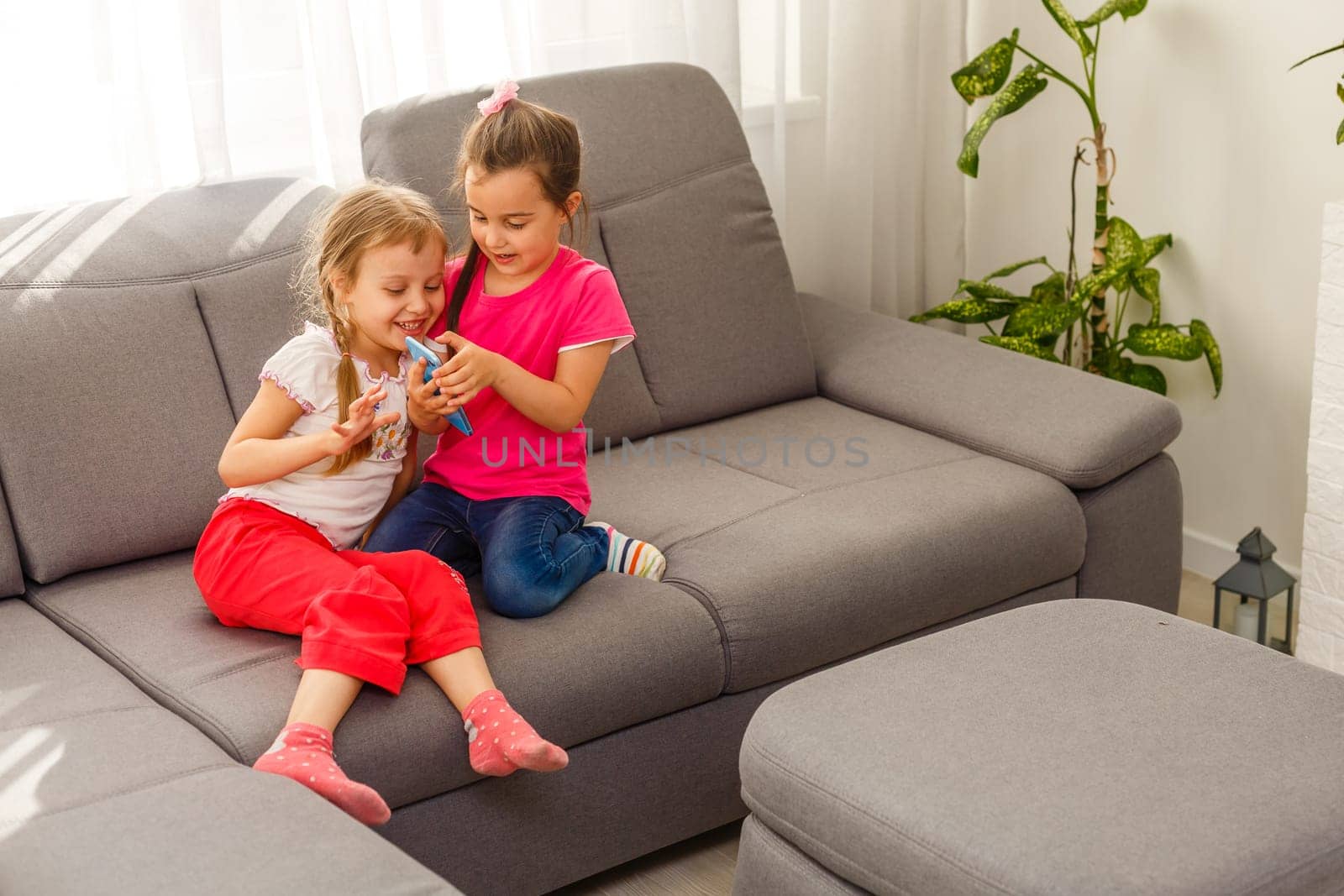 people, children, technology, friends and friendship concept - happy little girls sitting on sofa and taking selfie with smartphone at home. by Andelov13