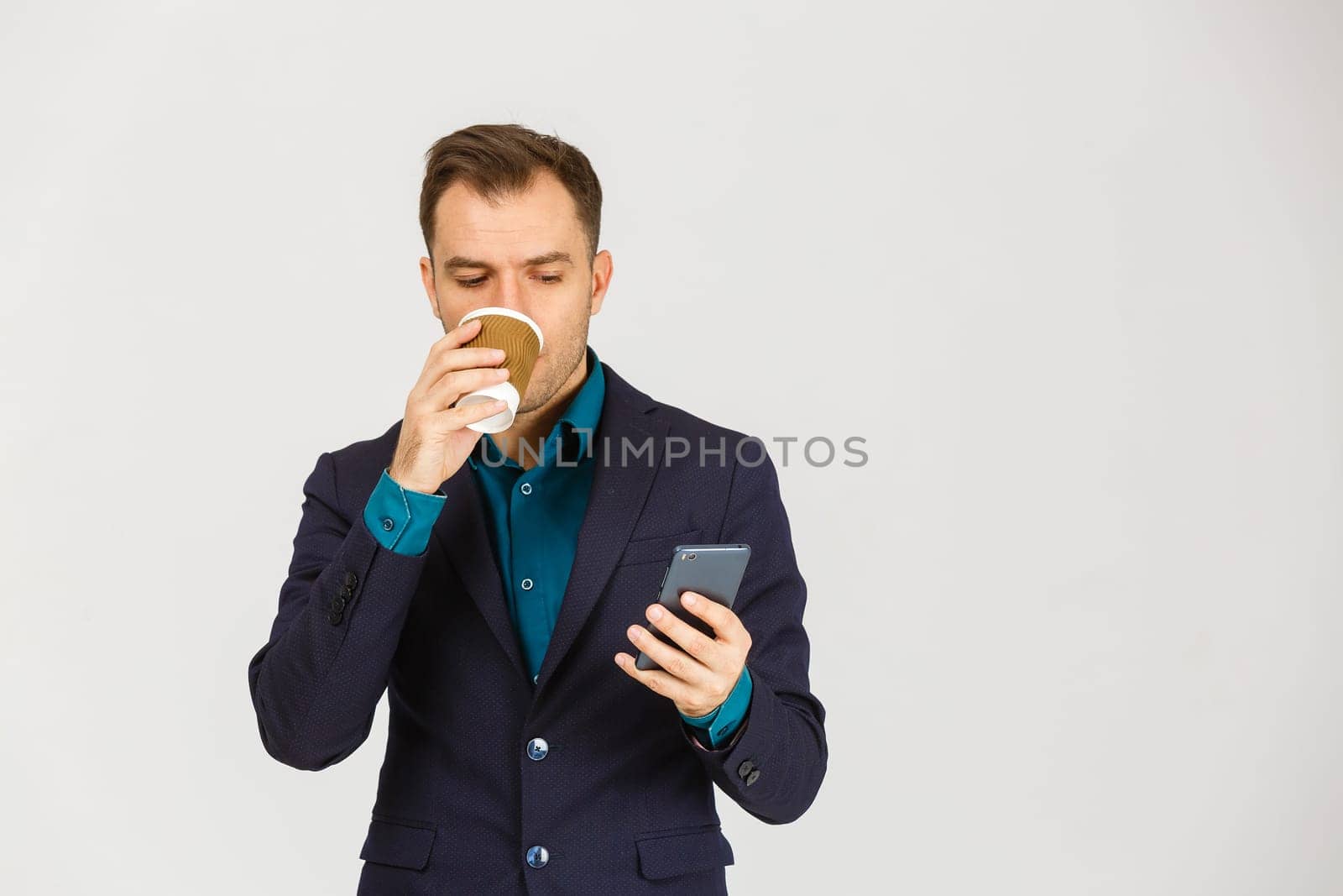 Confident young businessman using cell phone and drinking coffee.