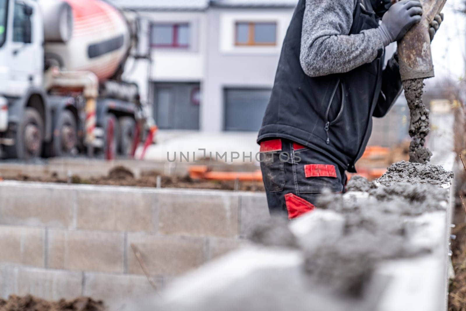 pouring concrete from the mixer truck hose into the base plate of the house.