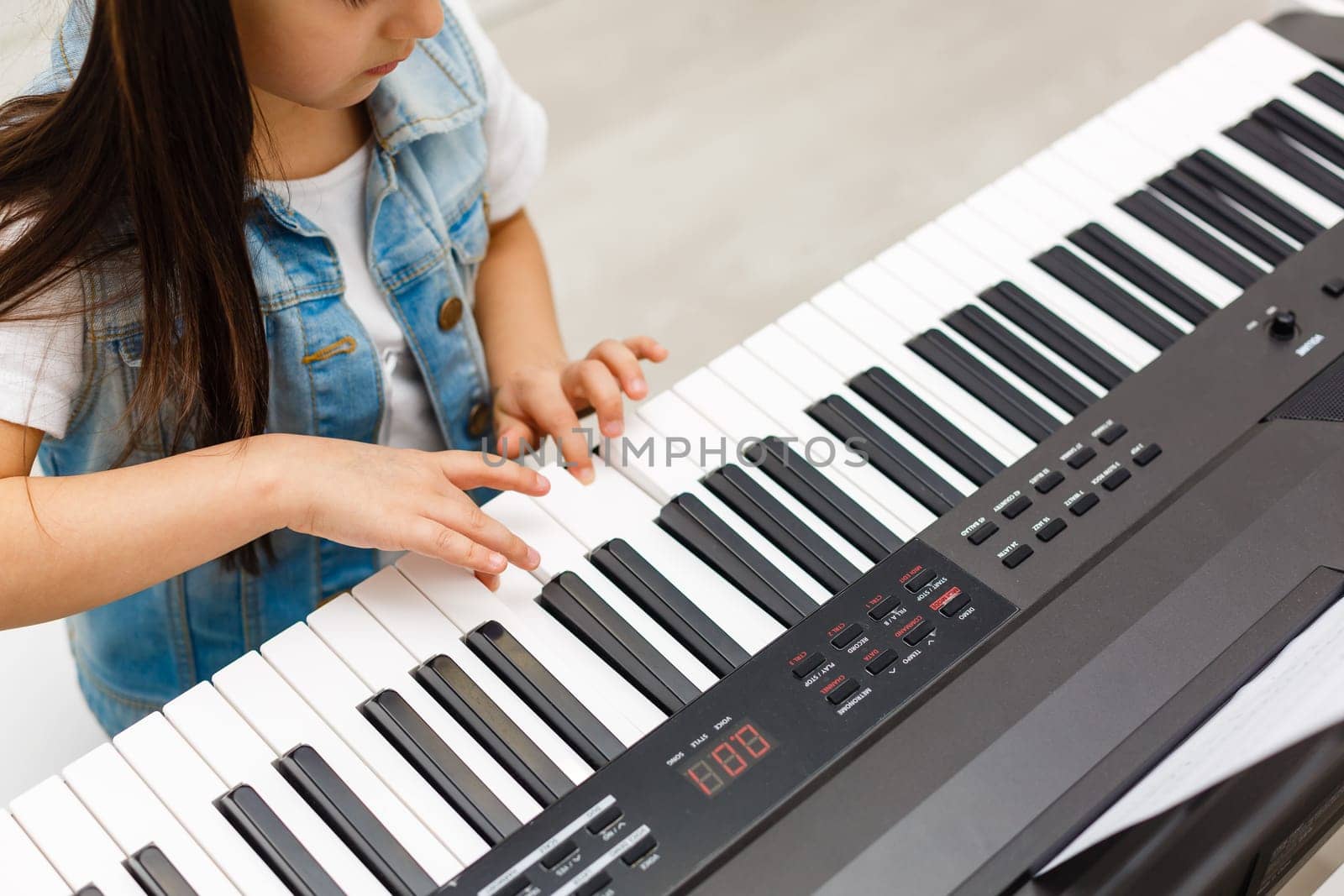 Cute little girl plays on piano, synthesizer. Training. Education. School. Aesthetic training. Elementary classroom.
