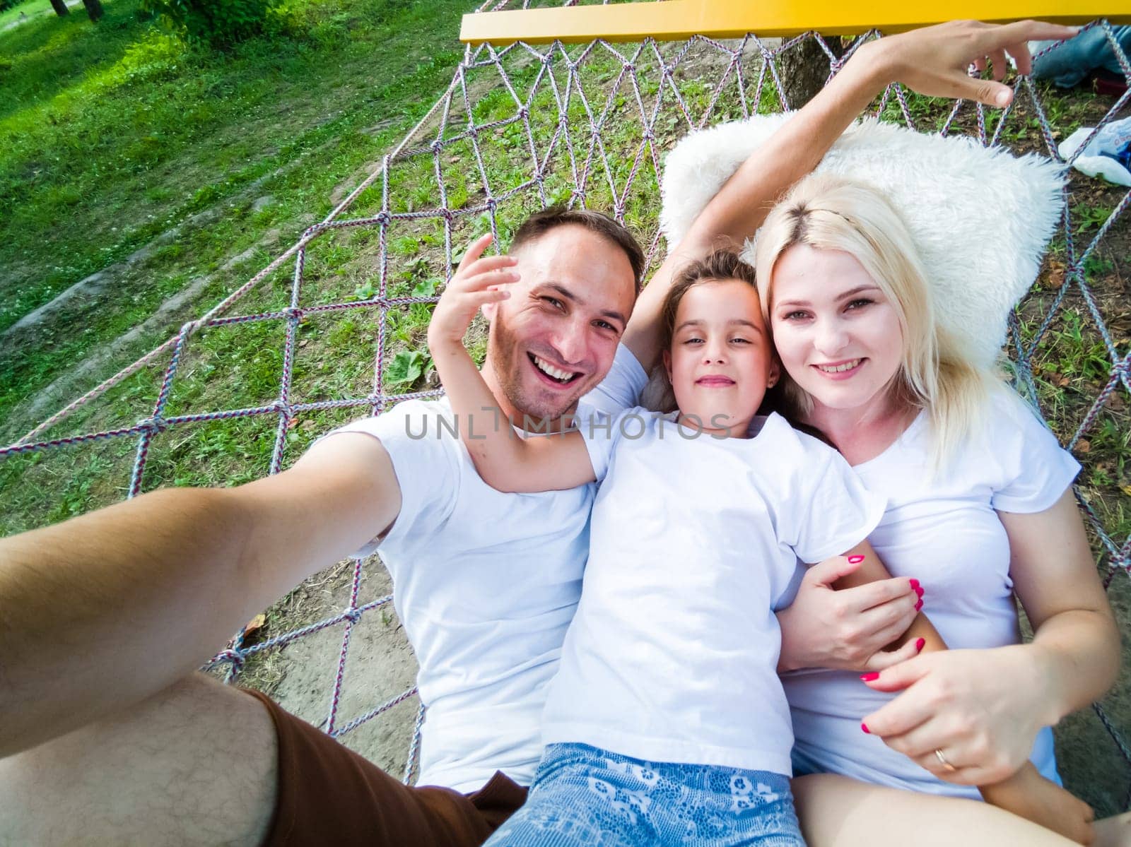 family laying down and relaxing together on a hammock during a sunny summer day on holiday home garden. Family relaxing outdoors, healthy and wellness lifestyle