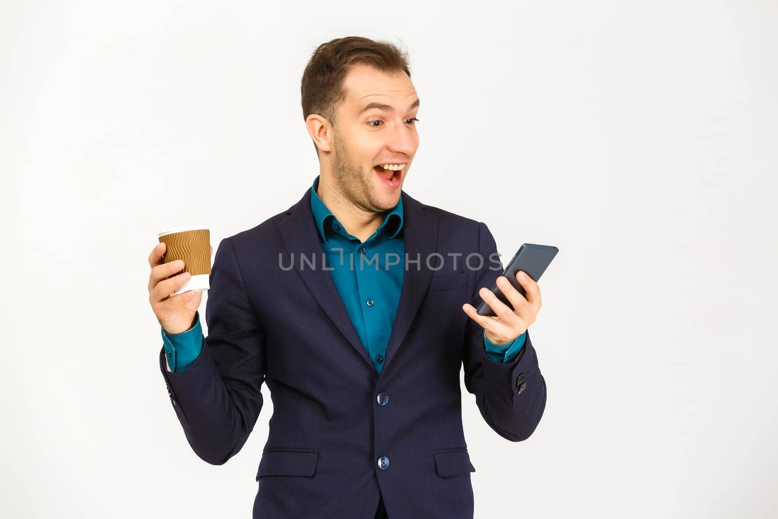 Portrait of a smiling young business man using smartphone and holding cup of coffee isolated on a white background by Andelov13