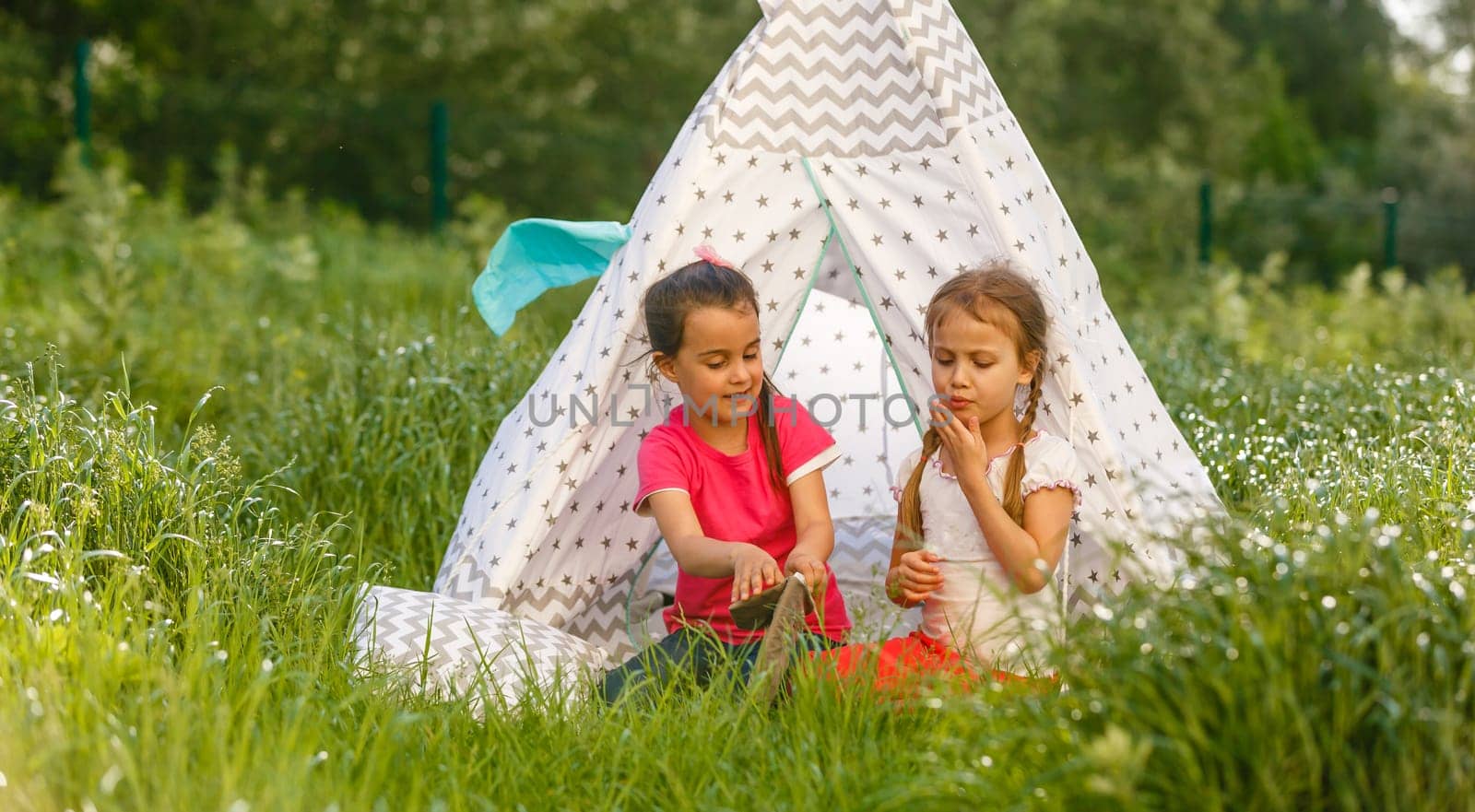 childhood and hygge concept - happy little girls playing in kids tent.