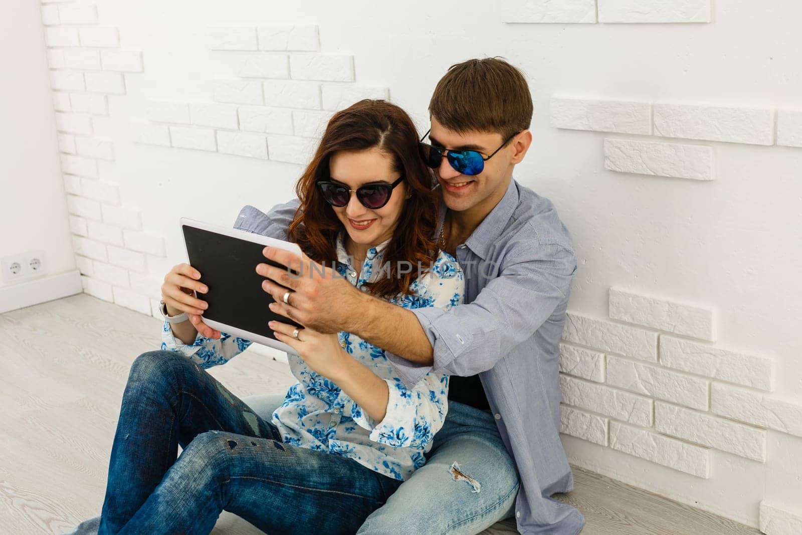 Simple happiness. Cheerful lovely couple cuddling on sofa at home, using digital tablet for websurfing, free space by Andelov13