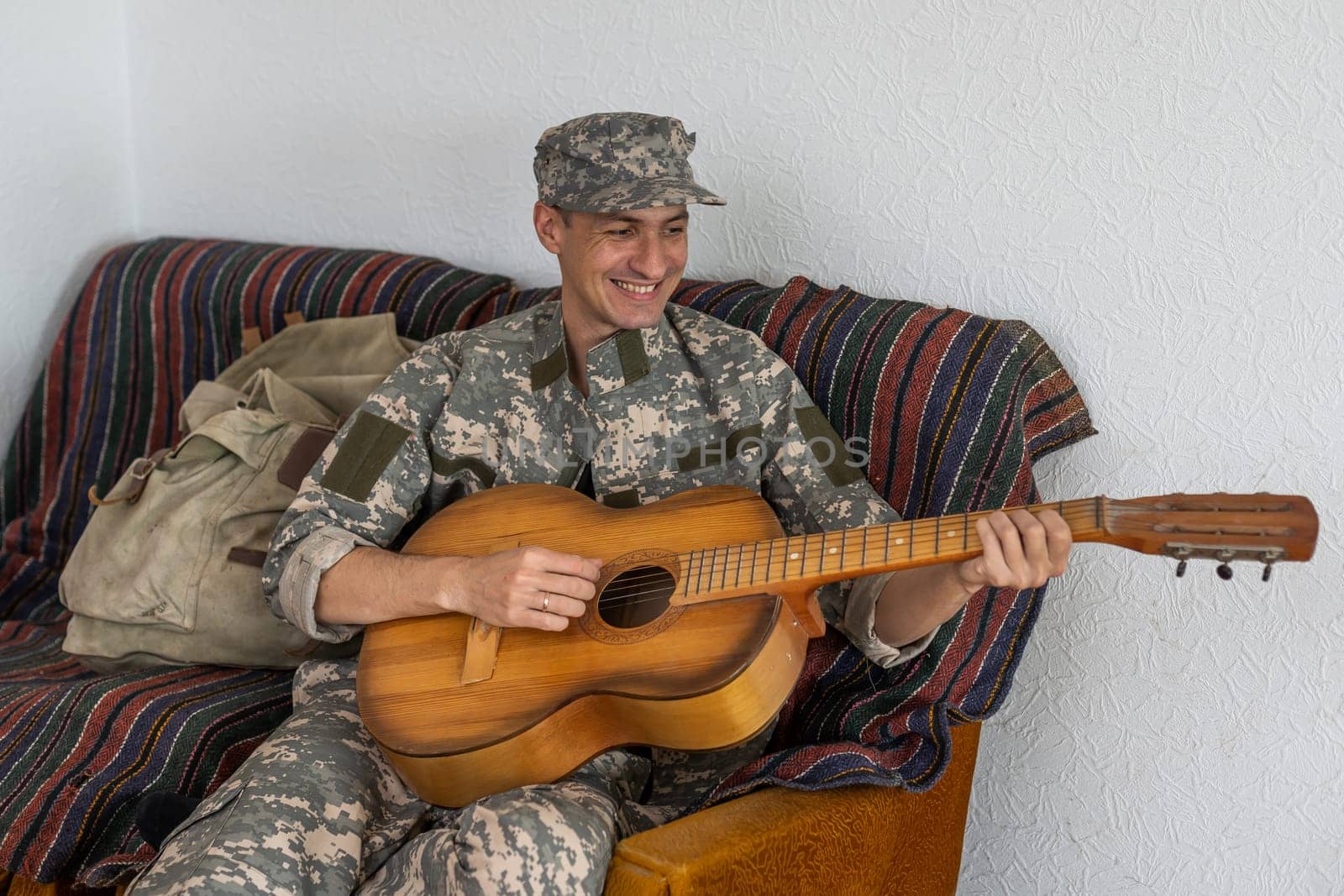 Cheerful smiling young military man wearing khaki uniform holding guitar