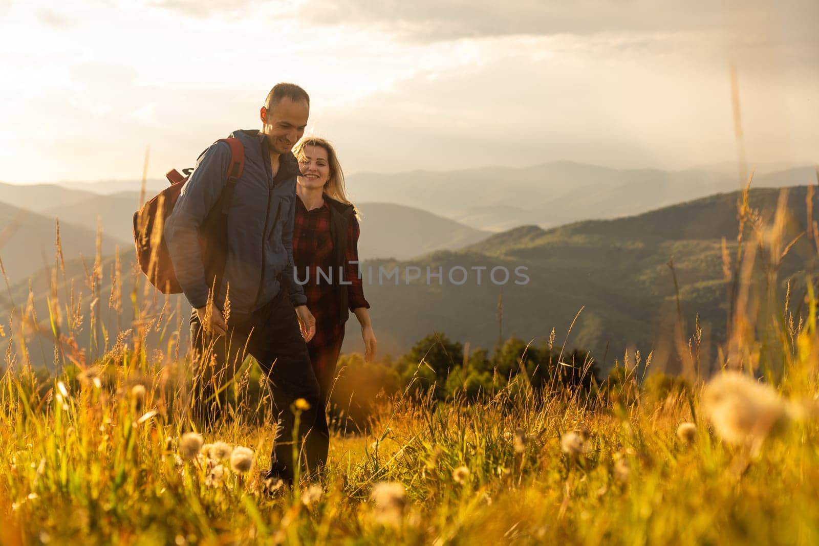 A man and a woman in tourist equipment are standing on a rock and admiring the panoramic view. A couple in love on a rock admires the beautiful views. A couple in love is traveling. A couple on a hike