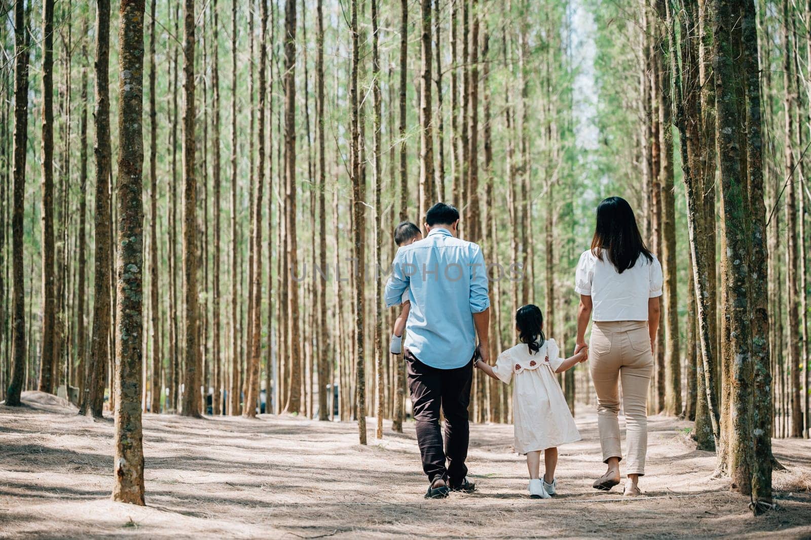 Asian man and a woman holding their baby and little kid walking through the forest on a sunny day, Happy family day