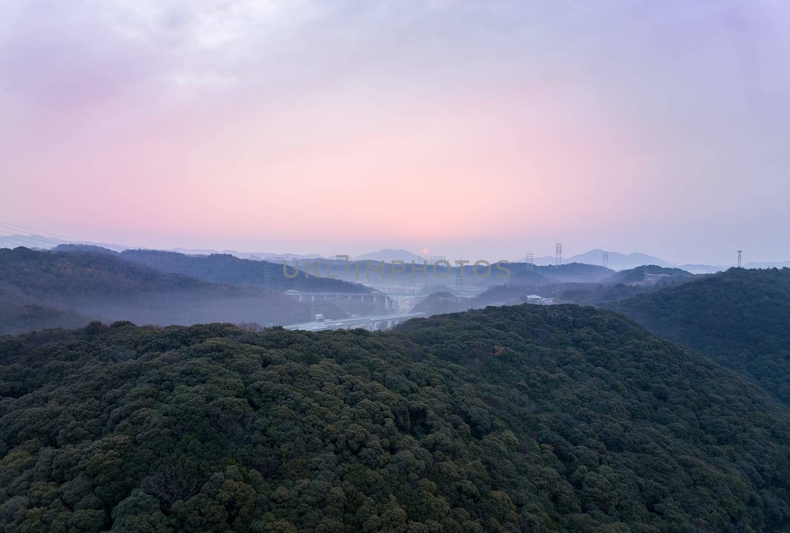 Distant early morning sun lights sky pink over misty hilly landscape by Osaze