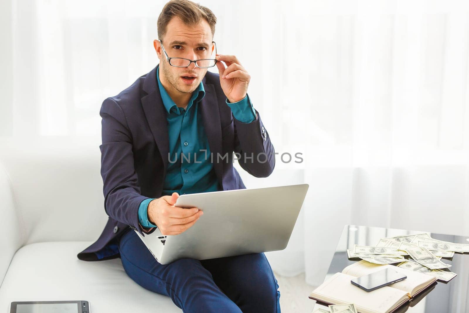 Multitasking. Handsome young man wearing glasses and working with touchpad while sitting on the couch in office
