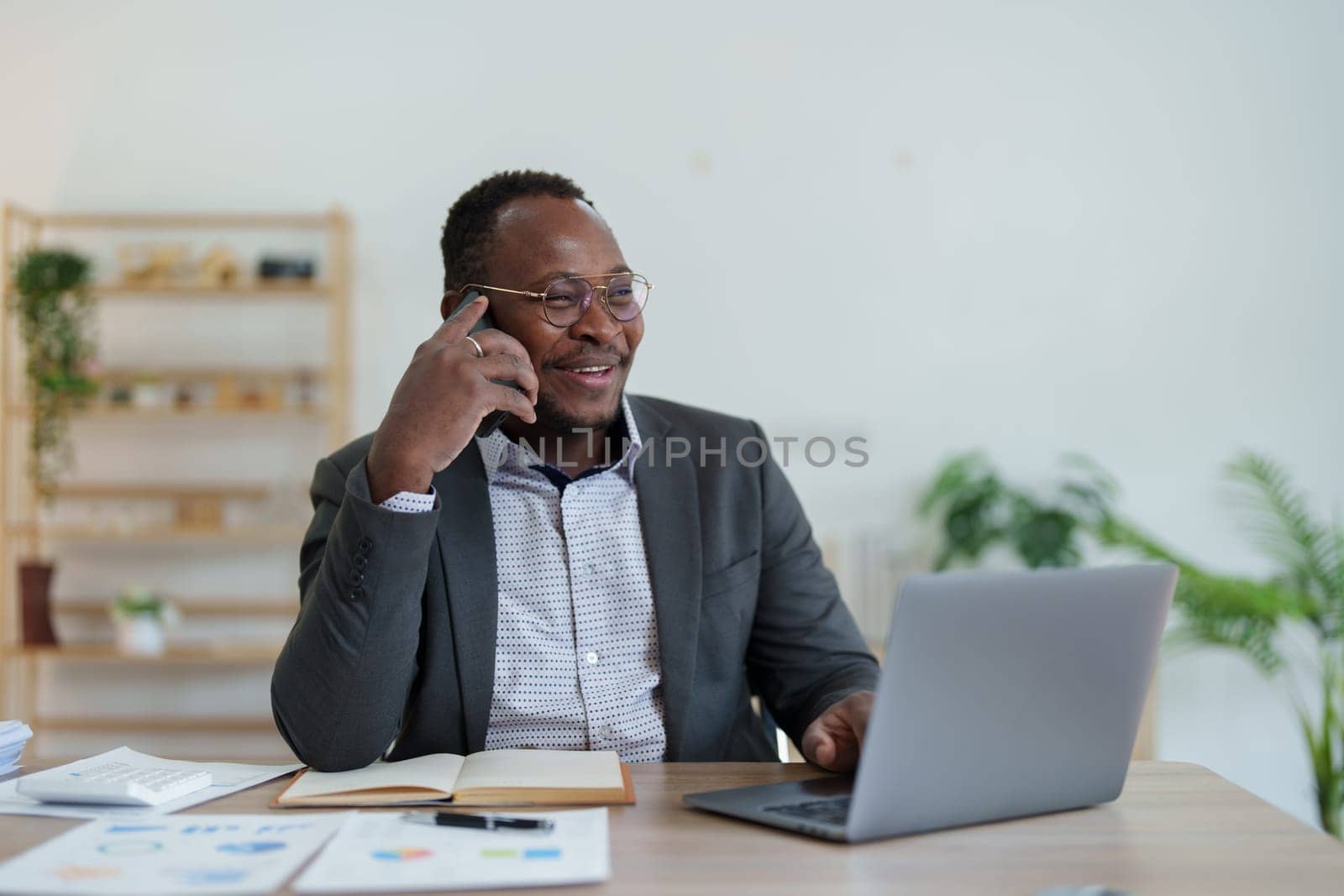 middle aged man American African using smart phone mobile and laptop computer with planning working on financial document, tax, exchange, accounting and Financial advisor by Manastrong