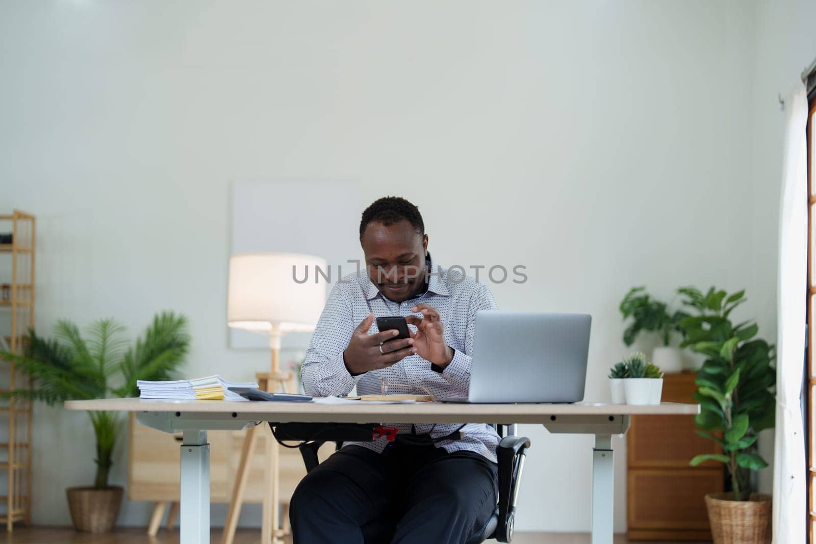 middle aged man American African using smart phone mobile and laptop computer with planning working on financial document, tax, exchange, accounting and Financial advisor by Manastrong