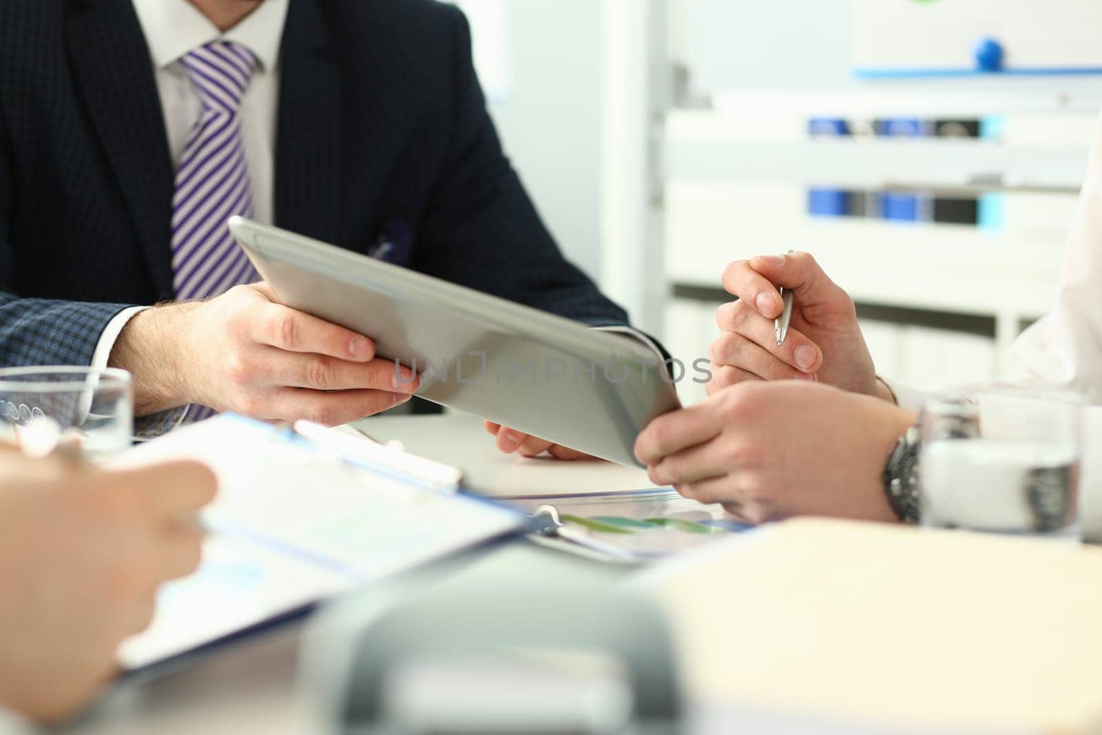 Businessmen talking using digital tablet sitting at office table. Male team two men work looking at technology device touchpad screen