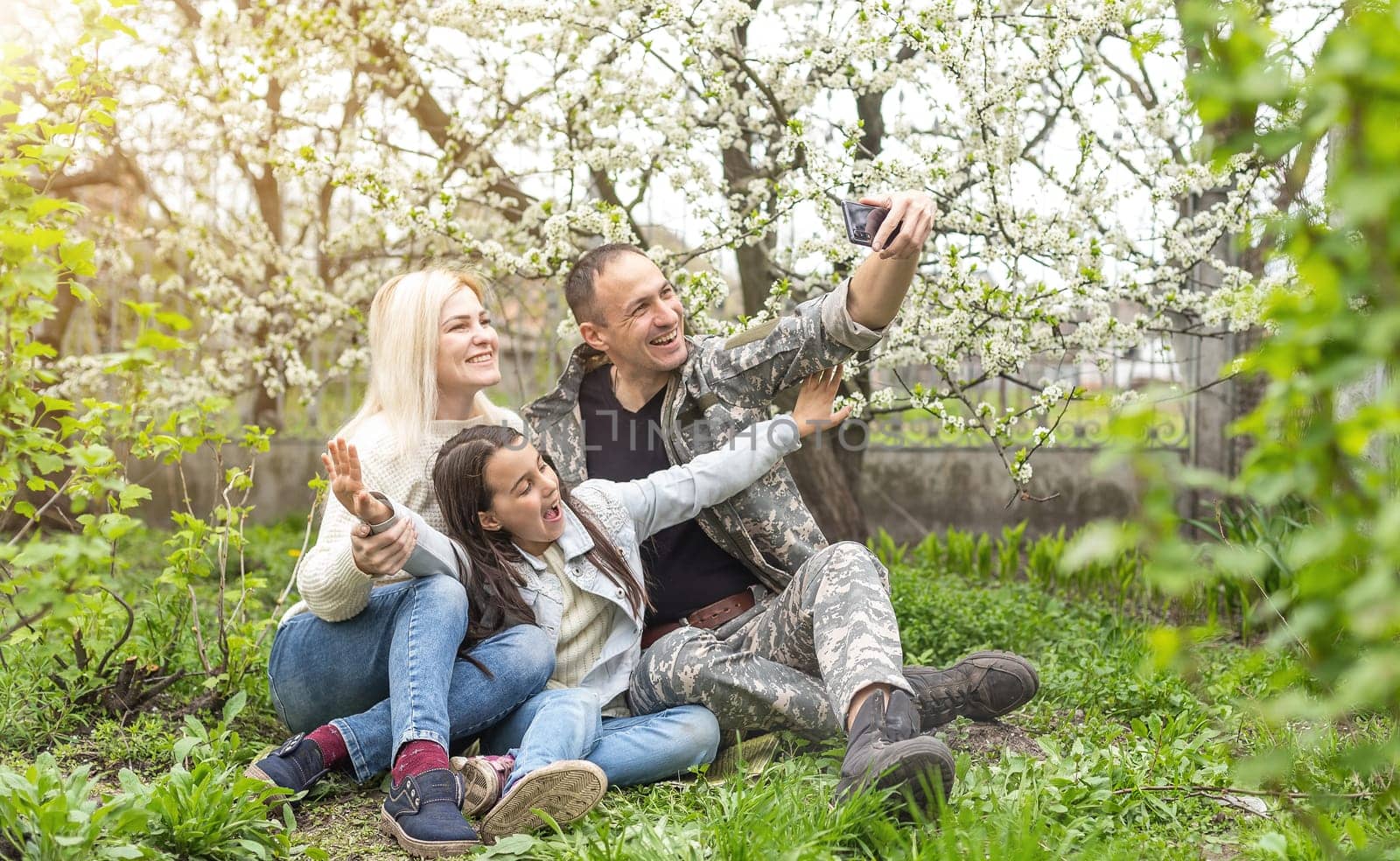 Soldier is meeting his family outdoors. Happy reunion of father and kids on the grass.