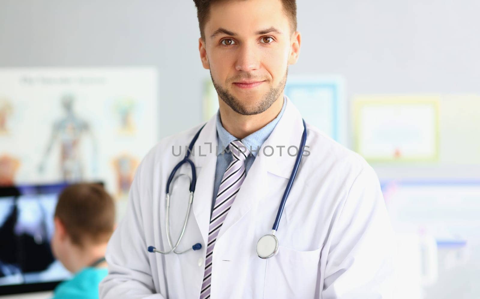 Portrait of smiling young doctor with a stethoscope on background of office in clinic. Medical services and insurance