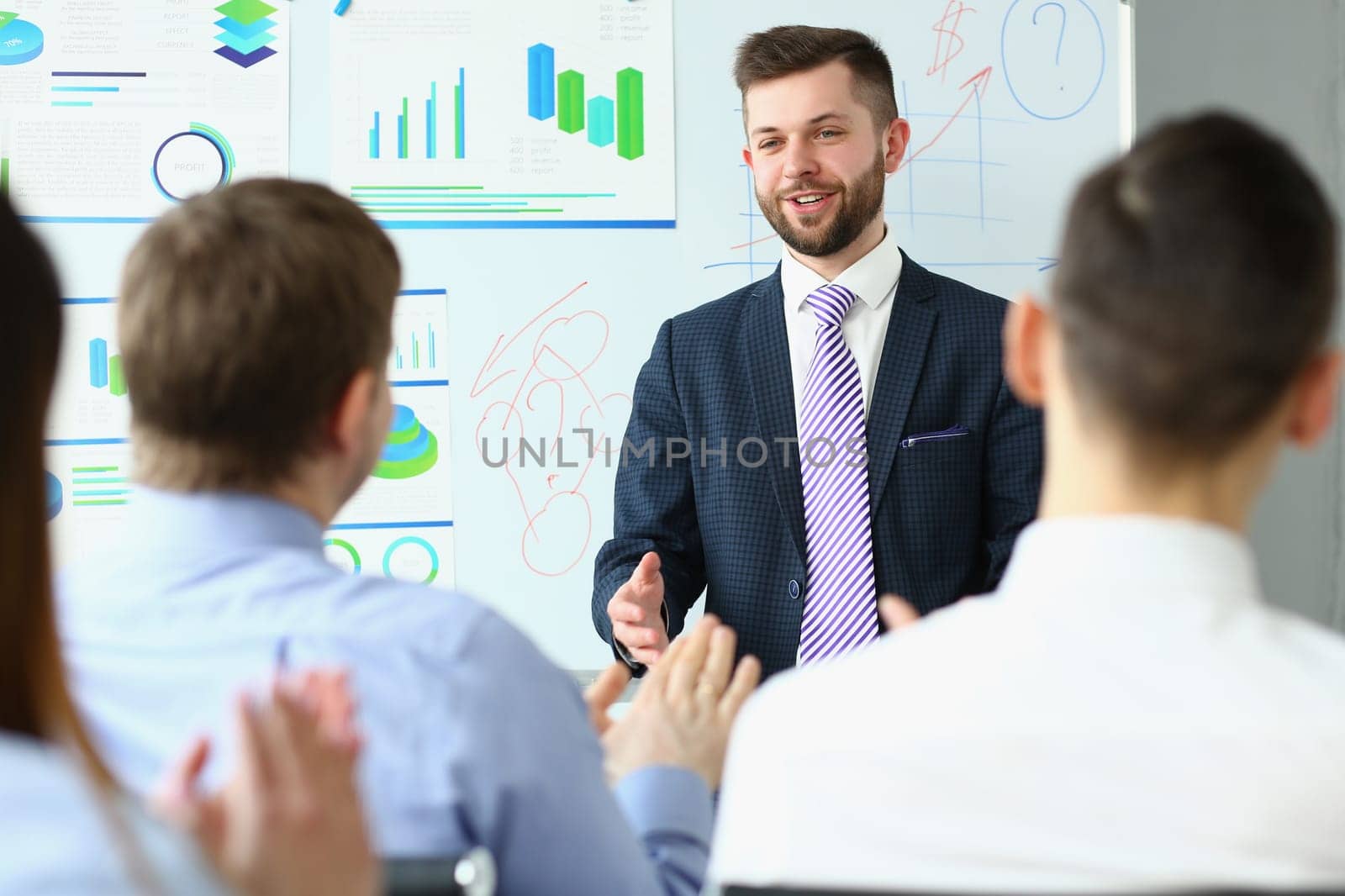 Male business coach speaker in suit makes presentation on white board. Male speaker advising on training and persuading client group employees