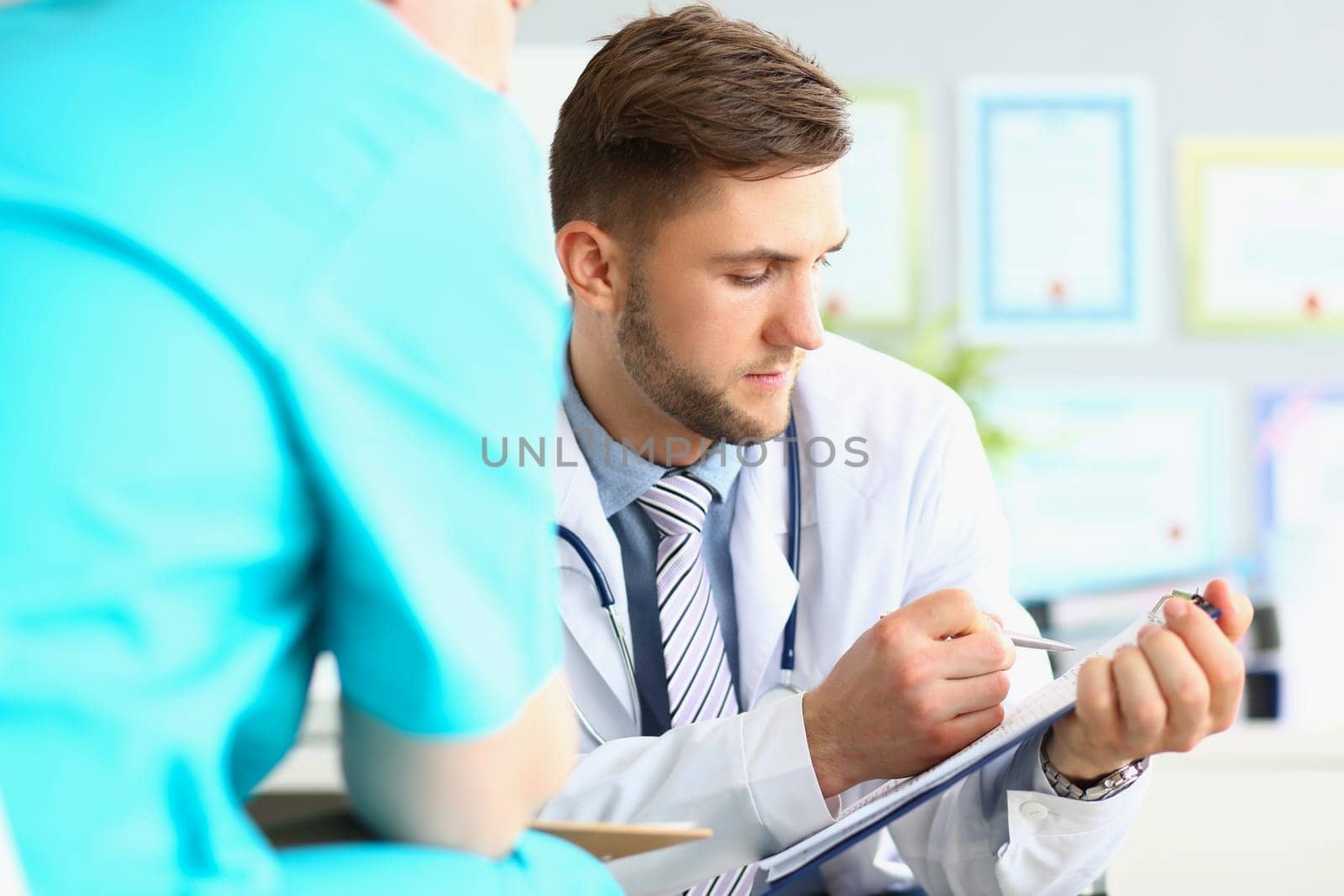 Male doctor looks at patient medical record in clinic. Medical insurance examination and diagnosis concept
