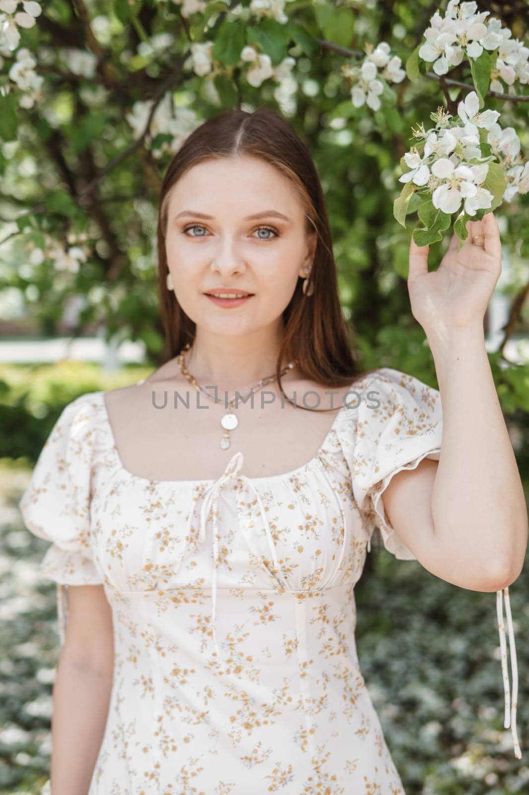 An attractive long-haired woman walks in the spring in the park of blooming apple trees. Spring portrait of a woman