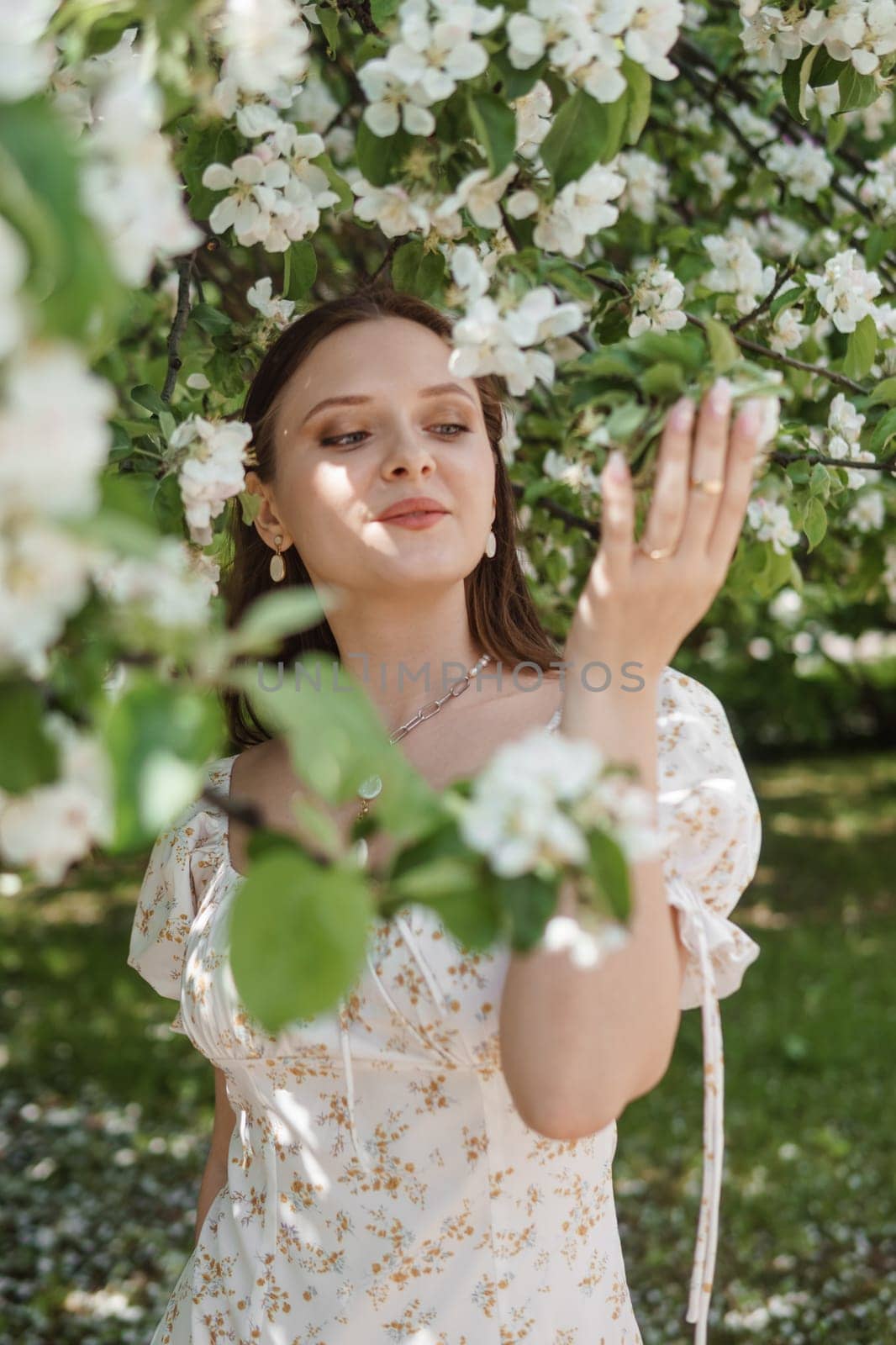 An attractive long-haired woman walks in the spring in the park of blooming apple trees. Spring portrait of a woman