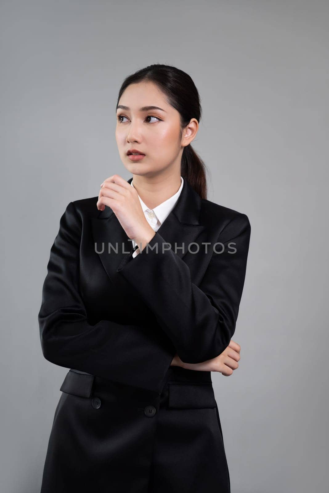 Confident young businesswoman stands on isolated background, posing in formal black suit. Office lady or manager with smart and professional appearance. Enthusiastic