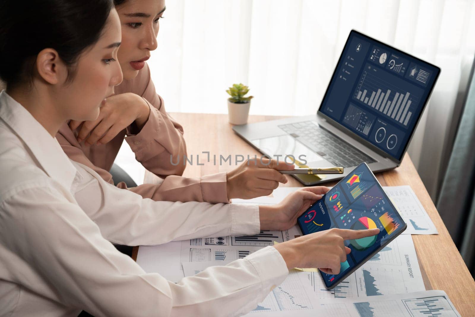 Analyst team colleague discuss financial data on digital dashboard, analyzing charts graph display on laptop and tablet screen. Modern office use business intelligence to plan marketing. Enthusiastic