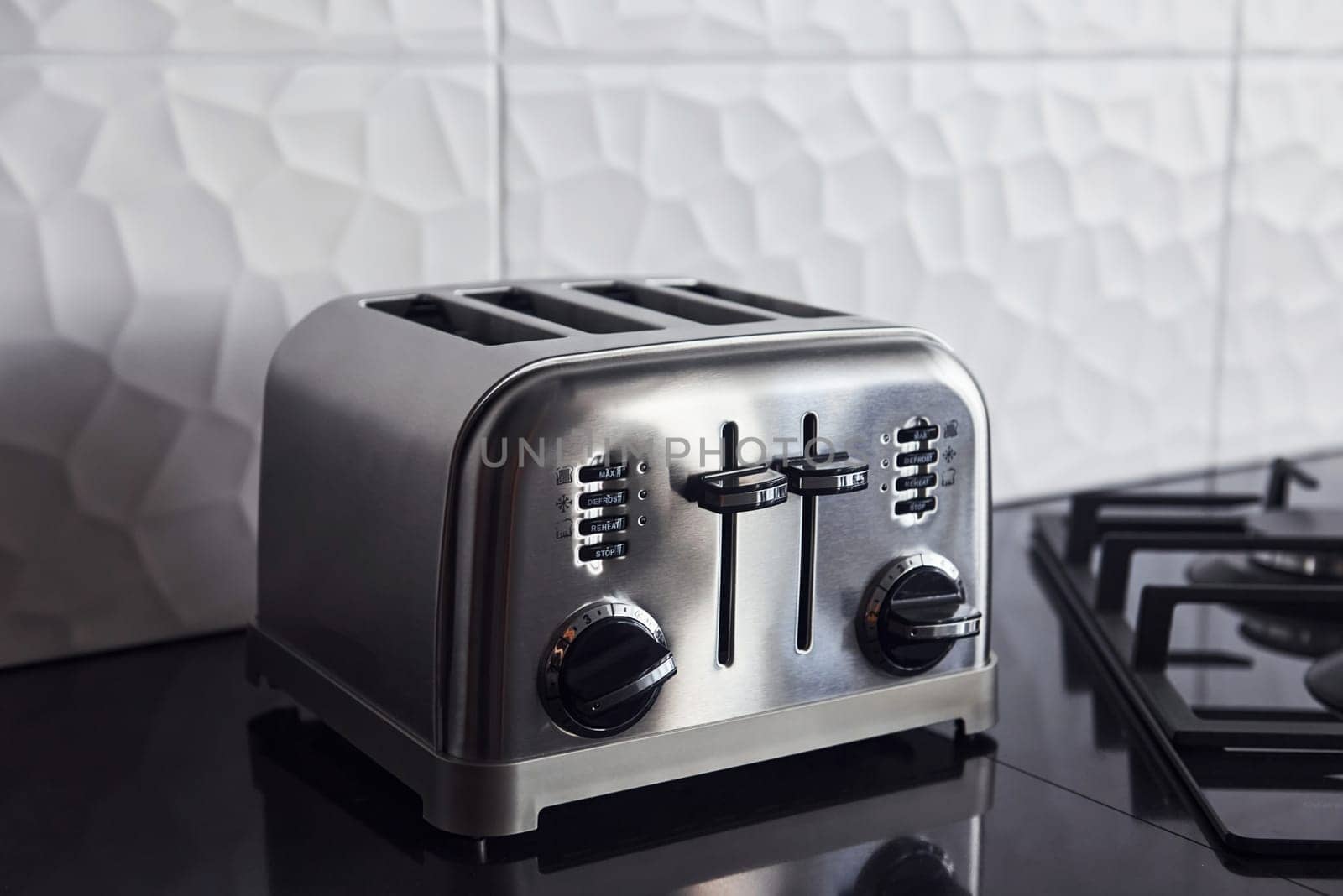 Close up view of silver colored toaster that standing on gas stove indoors in kitchen.