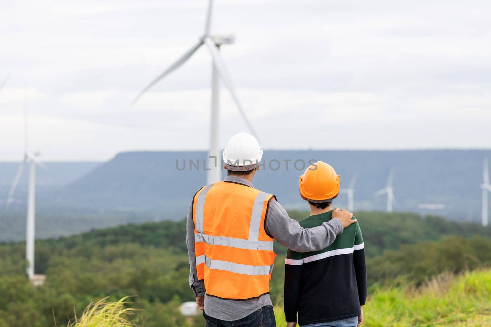 Engineer with his son on a wind farm atop a hill or mountain in the rural. Progressive ideal for the future production of renewable, sustainable energy. Energy generation from wind turbine.